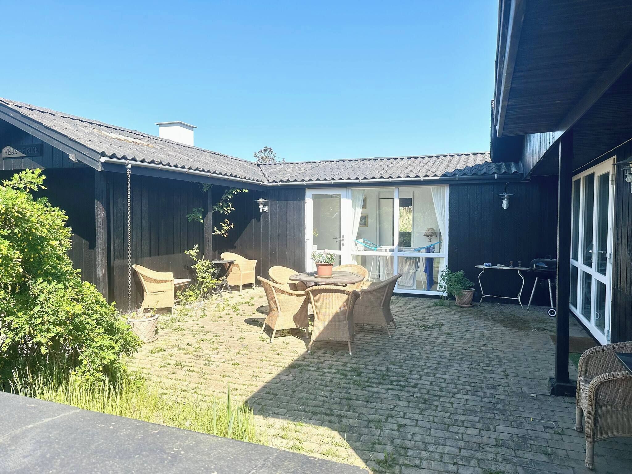 Een overdekt terras buiten met rieten meubilair, een terrasvloer van baksteen en uitzicht op het huis.