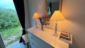 Una habitación con un aparador blanco, dos lámparas, un florero con flores y un espejo.