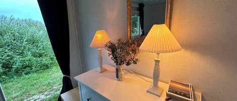 A room with a white dresser, two lamps, a vase with flowers, and a mirror.