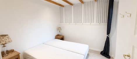 A bedroom with a bed, a nightstand, a lamp, a window with blinds, and a door with a handle.