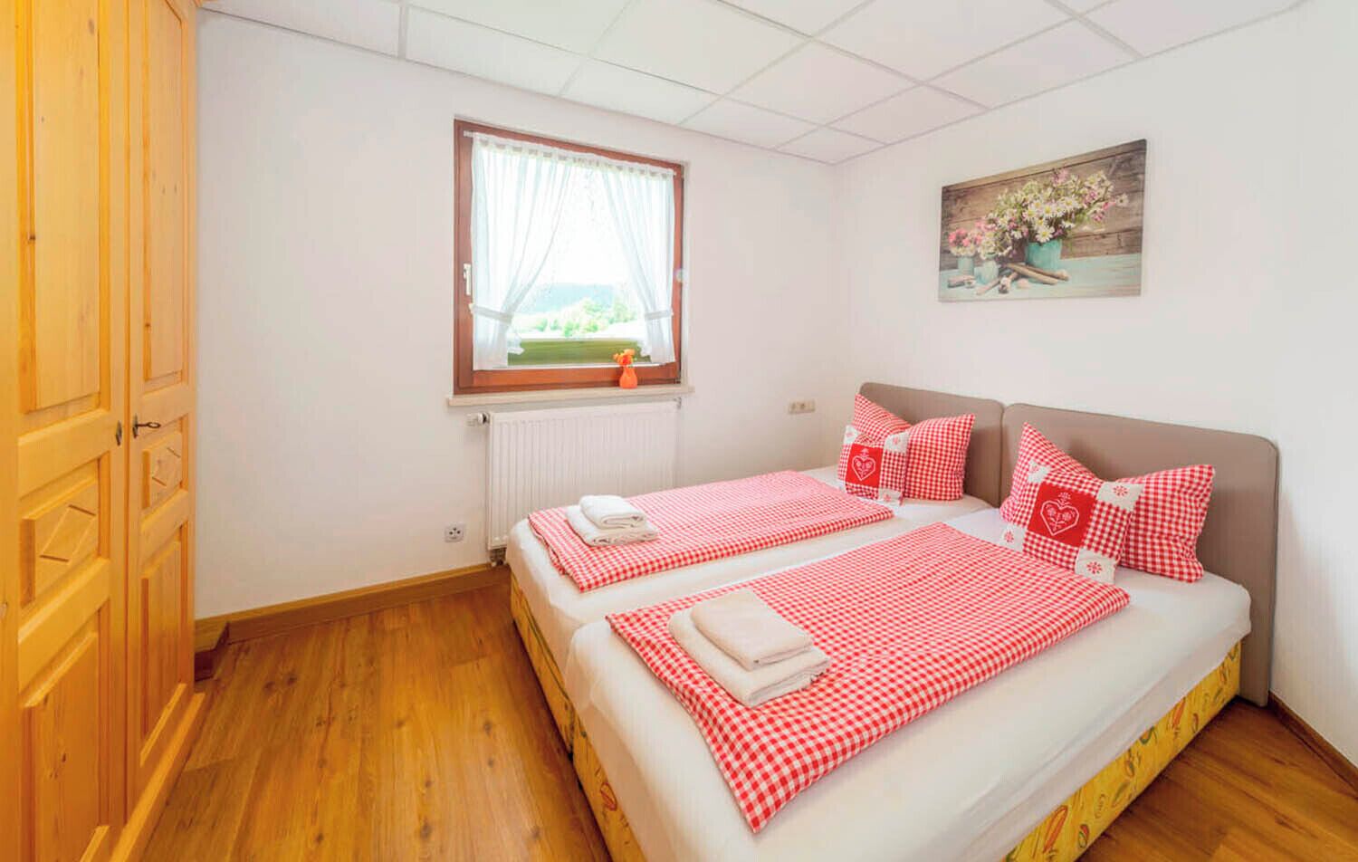 Een slaapkamer met twee bedden, een raam met gordijnen, een radiator en een schilderij aan de muur.