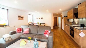 Ein modernes Wohnzimmer mit grauem Sofa, Couchtisch und Küchenzeile mit Holzausbau und Herd.