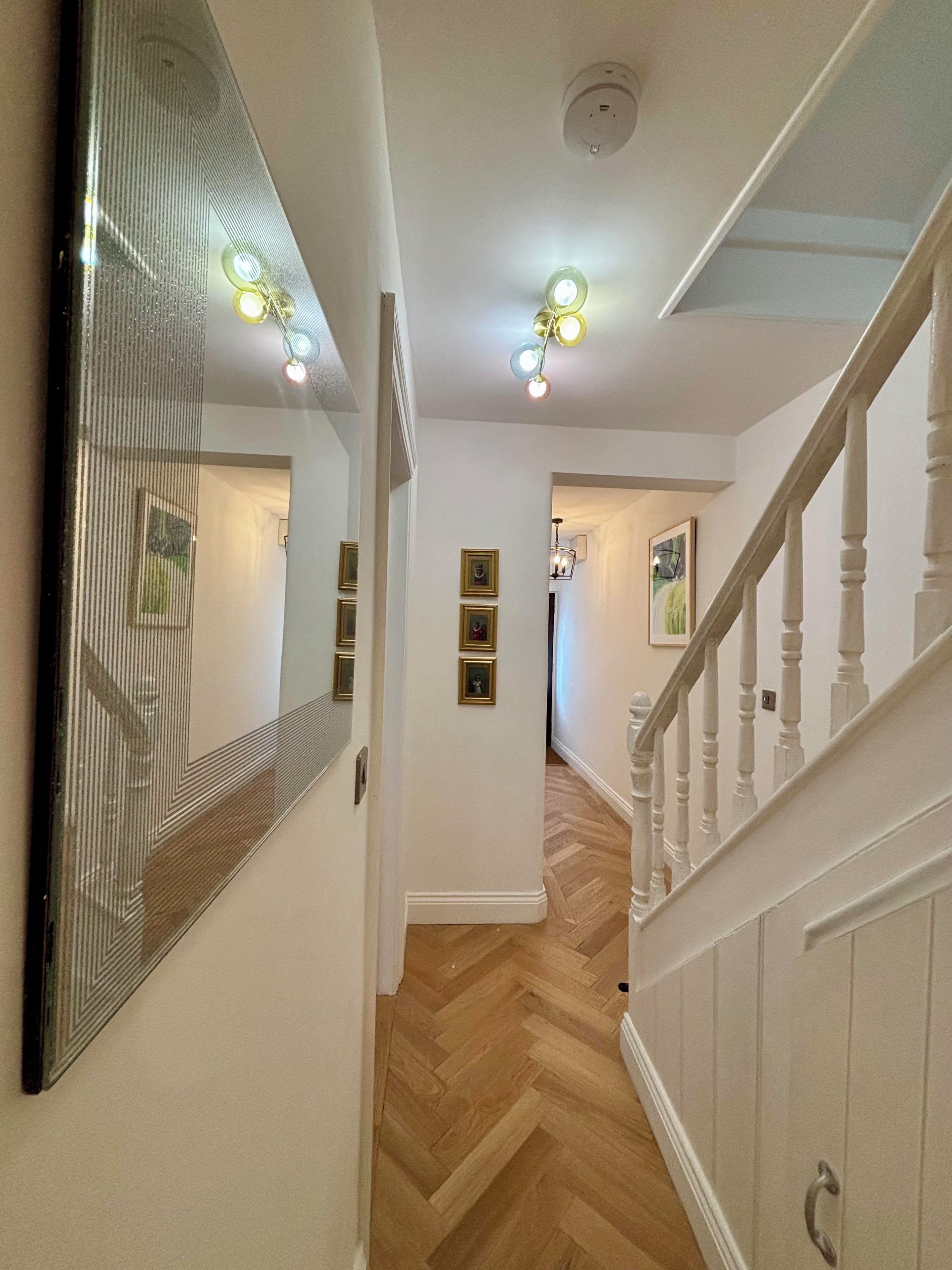A hallway with a wooden herringbone floor, a white railing, and a ceiling light fixture.