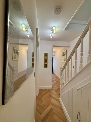 A hallway with a wooden herringbone floor, a white railing, and a ceiling light fixture. - Stunning 4BR Brighton House - Near Beach & Lanes (Brighton)