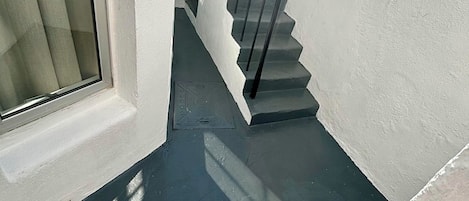 A narrow stairway with a metal railing leading to a landing, surrounded by white walls.