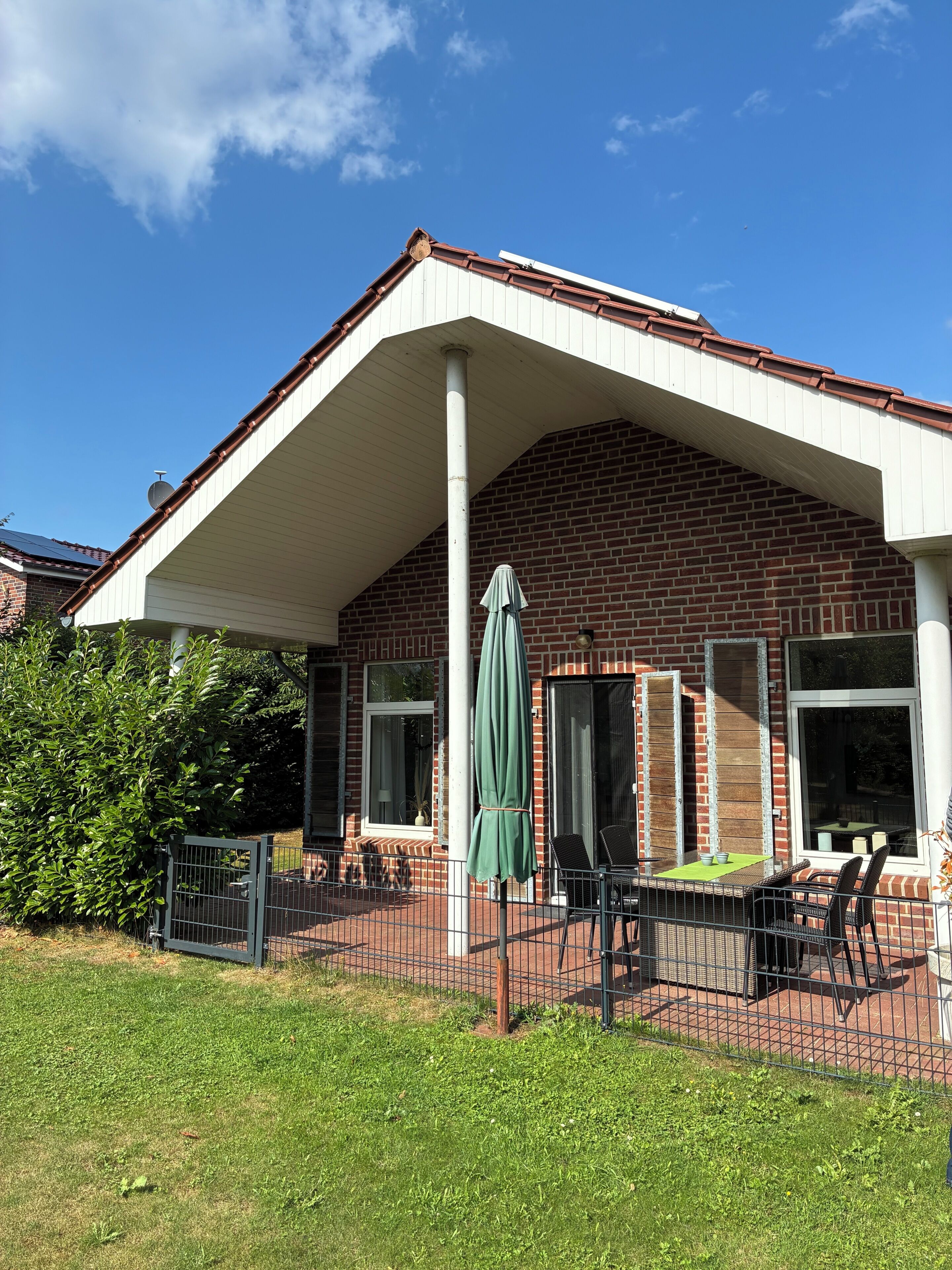 A brick building with a covered patio area, a fenced garden, and a green umbrella.