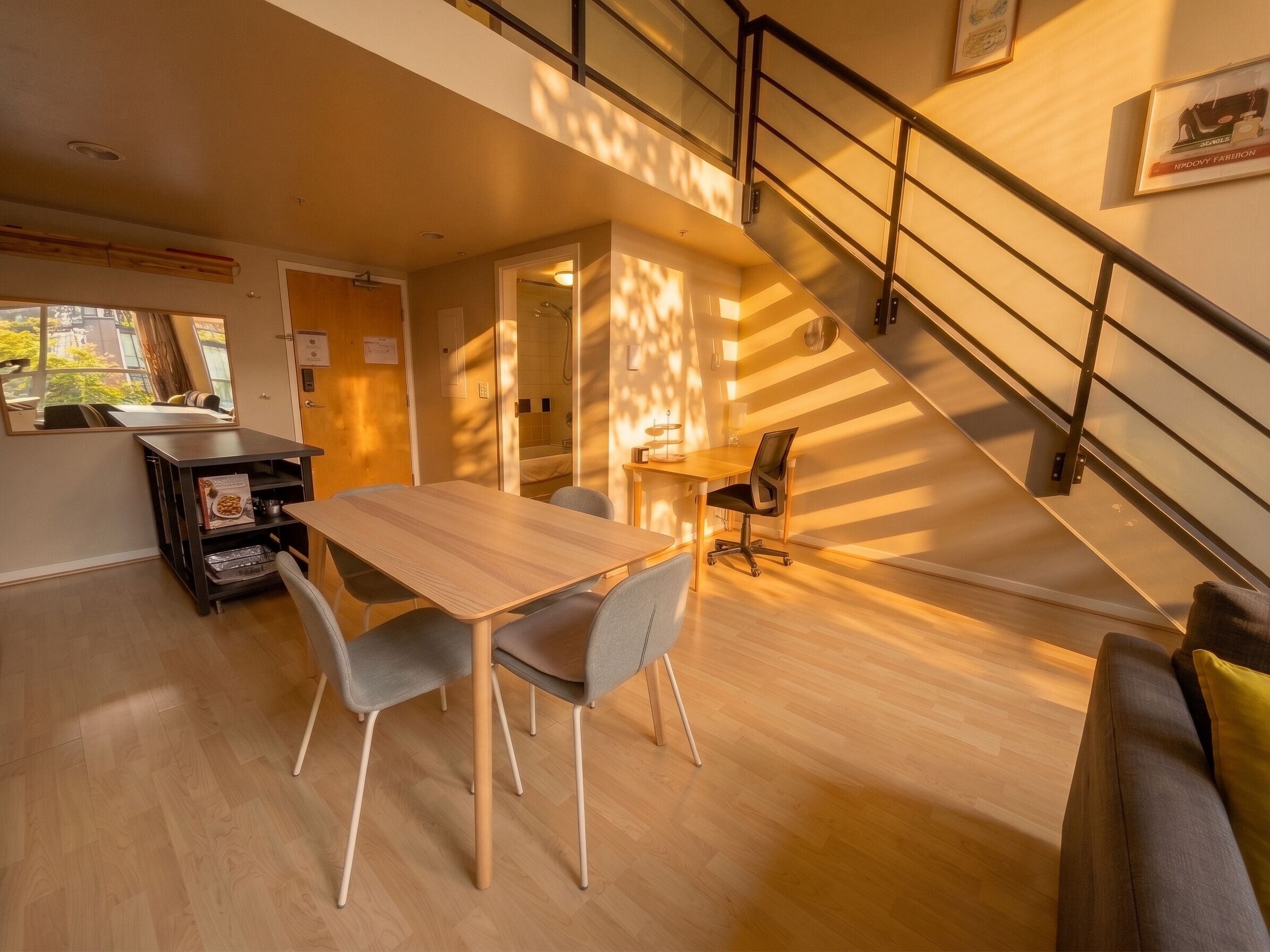 Um interior moderno com uma mesa de jantar de madeira, cadeiras cinzentas, uma escada e vista para o exterior.