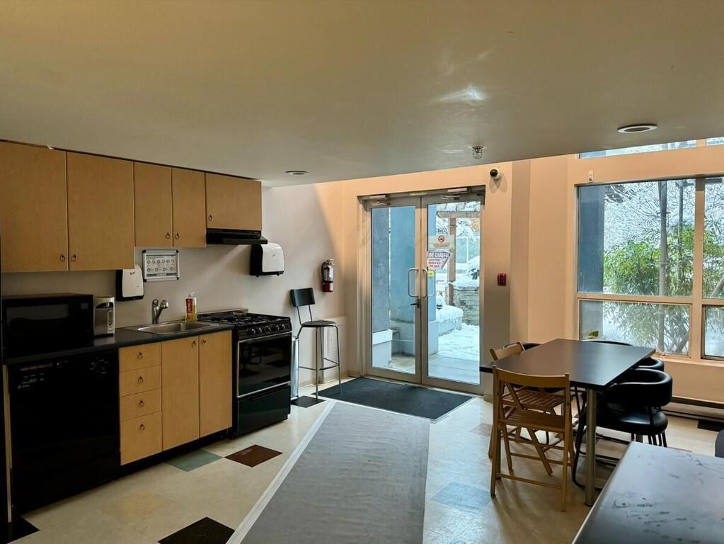 A modern kitchen with wooden cabinets, a black dishwasher, and a stove. There is a dining area with a table and chairs.