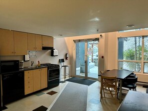 A modern kitchen with wooden cabinets, a black dishwasher, and a stove. There is a dining area with a table and chairs. - Urban Loft Nook • City Views• Free Parking (Vancouver)