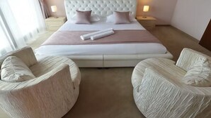 Una camera d'albergo con un letto grande, due comodini, due poltrone imbottite e una finestra con tende.
