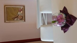 Una stanza con un quadro appeso al muro, una sedia bianca e un oggetto decorativo con un fiocco.