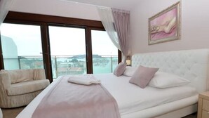 Un dormitorio con una cama grande, una silla, una mesita de noche y un cuadro en la pared.