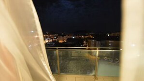 Nachtsicht von einem Balkon mit Geländer, mit Blick auf eine Stadtlandschaft aus Gebäuden und Lichtern.