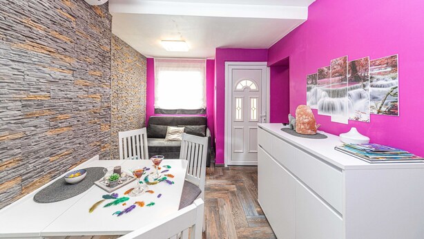 Un espacio habitable compacto con una pared de piedra, una kitchenette, un área de comedor con una mesa dispuesta para dos personas y un sofá.