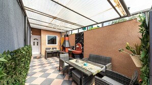 Un patio al aire libre con piso a cuadros, muebles de mimbre, una parrilla y una planta en maceta.