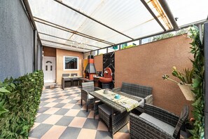Eine Terrassengruppe im Freien mit Schachbrettmuster-Boden, Korbmöbeln, einem Grill und einem Blumentopf.
