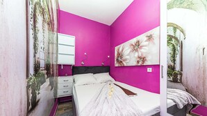 Un dormitorio con una cama, una mesita de noche, un espejo y un cuadro floral en la pared.