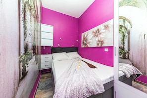 Ein Schlafzimmer mit einem Bett, einem Nachttisch, einem Spiegel und einer Wand mit einem floralen Gemälde.