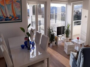 A modern living room with a dining area, large windows, and a painting of sailboats. - Villa Nika-five Bedroom Villa With Pool (Zupa dubrovacka)