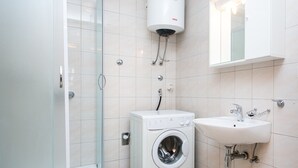 A modern bathroom with a glass-enclosed shower, a built-in washing machine, and a sink with a mirror above it. - Apartments Radic - Studio Apartment - Kneza Domagoja Street - BR 1 (Dubrovnik)
