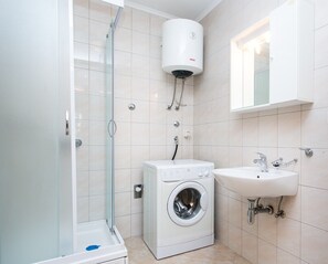 Ein modernes Badezimmer mit einer gläsernen Dusche, einer integrierten Waschmaschine und einem Waschbecken mit Spiegel darüber.