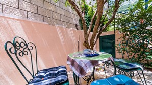 An outdoor seating area with metal chairs and a table, surrounded by a low wall and greenery. - Apartments Casa Vanna - One Bedroom Apartment (Dubrovnik)