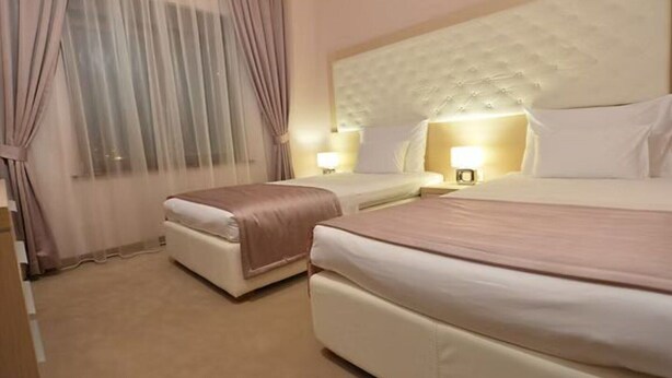 Ein Hotelzimmer mit zwei Betten, einem großen, gepolsterten Kopfteil und einem Fenster mit durchsichtigen Vorhängen.