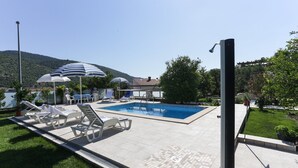 A swimming pool with lounge chairs and umbrellas, surrounded by greenery and a mountain in the background. - Villa Celenca - Superior Two Bedroom Apartment With Terrace and Sea View - A5 (Dubrovnik)