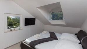 A bedroom with a bed, a television mounted on the wall, and a window with a view of greenery. - Villa Celenca - Superior Two Bedroom Apartment With Terrace and Sea View - A5 (Dubrovnik)