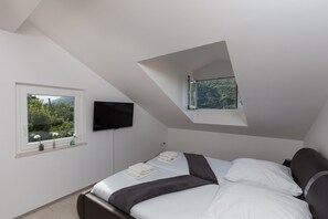 A bedroom with a bed, a television mounted on the wall, and a window with a view of greenery. - Villa Celenca - Superior Two Bedroom Apartment With Terrace and Sea View - A5 (Dubrovnik)