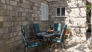 A stone-walled patio with a table and chairs, a window, and a potted plant. - Villa Celenca - Superior Two Bedroom Apartment With Terrace and Sea View - A5 (Dubrovnik)
