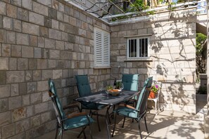 A stone-walled patio with a table and chairs, a window, and a potted plant. - Villa Celenca - Superior Two Bedroom Apartment With Terrace and Sea View - A5 (Dubrovnik)