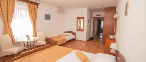A hotel room with two beds, a chair, a small table, and a window with curtains.