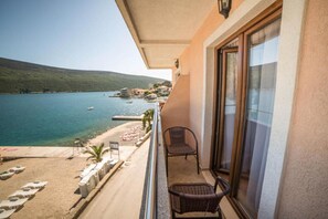 Un balcón con vista a un lago y una playa, dos sillas de mimbre y una mesita.