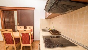 A compact kitchen with a stove, sink, and a dining area with chairs. - Fiammanti Hotel Montenegro-One Bedroom Apartment (Herceg Novi)