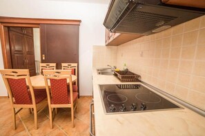 A compact kitchen with a stove, sink, and a dining area with chairs. - Fiammanti Hotel Montenegro-One Bedroom Apartment (Herceg Novi)