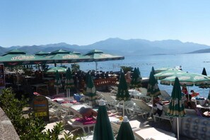 A seaside restaurant with outdoor seating and umbrellas, overlooking a body of water and mountains. - Fiammanti Hotel Montenegro-Standard Double Room Attick (Herceg Novi)
