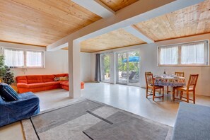 A spacious living area with a wooden ceiling, a red sofa, a dining table with chairs, and large windows. - Casa Maamii Mugena With Terrace And Parking (Alto Malcantone)