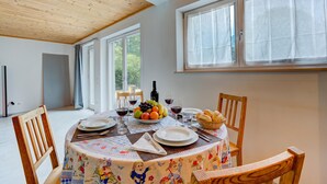 A dining area with a round table set for two, featuring a tablecloth with cartoon characters, a bowl of fruit, wine glasses, and a bottle of wine. - Casa Maamii Mugena With Terrace And Parking (Alto Malcantone)