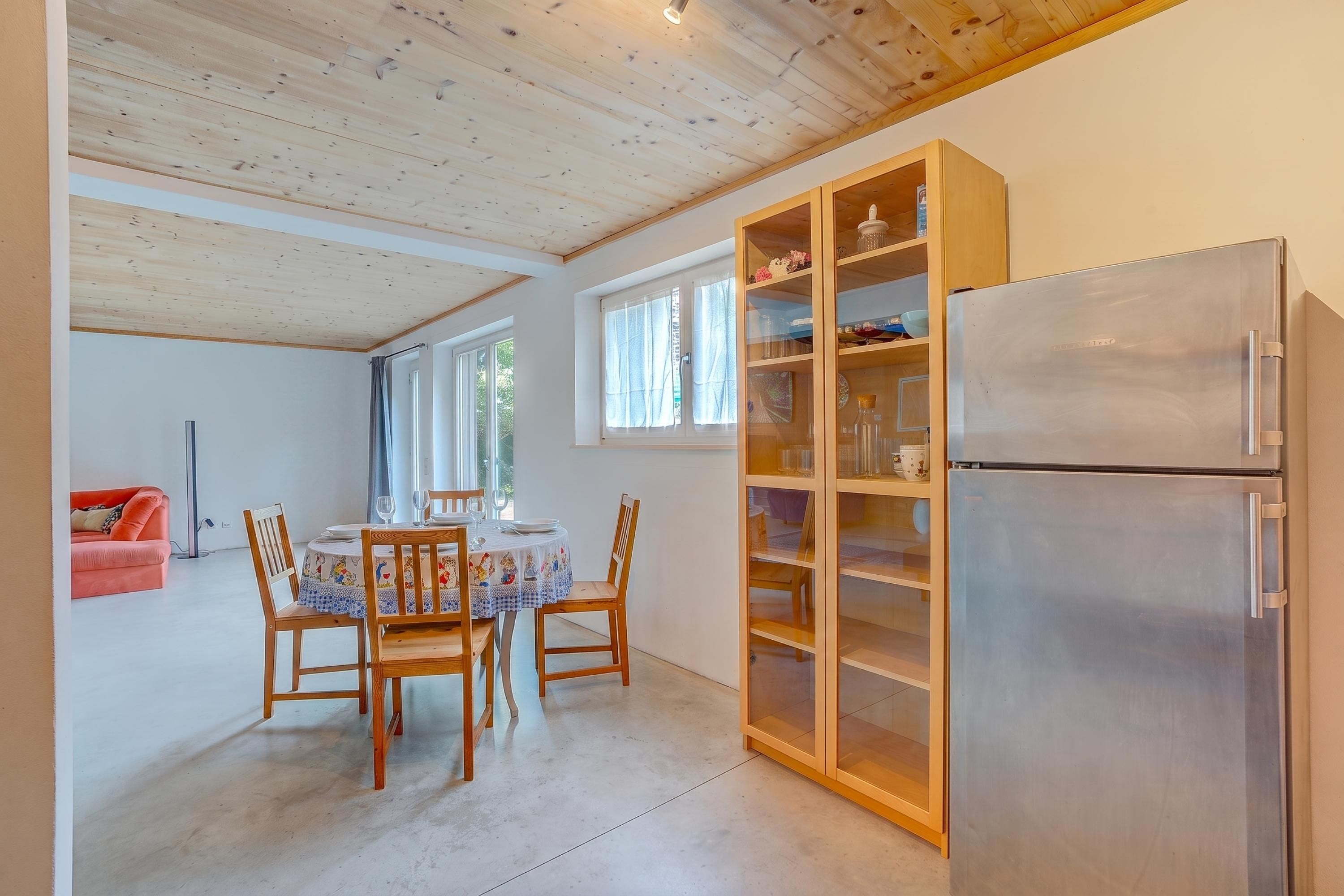 Una cocina con mesa, sillas, refrigerador y un armario con puertas de cristal.