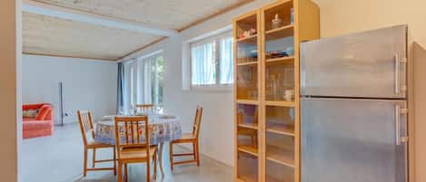 A kitchen with a dining table, chairs, a refrigerator, and a cabinet with glass doors.