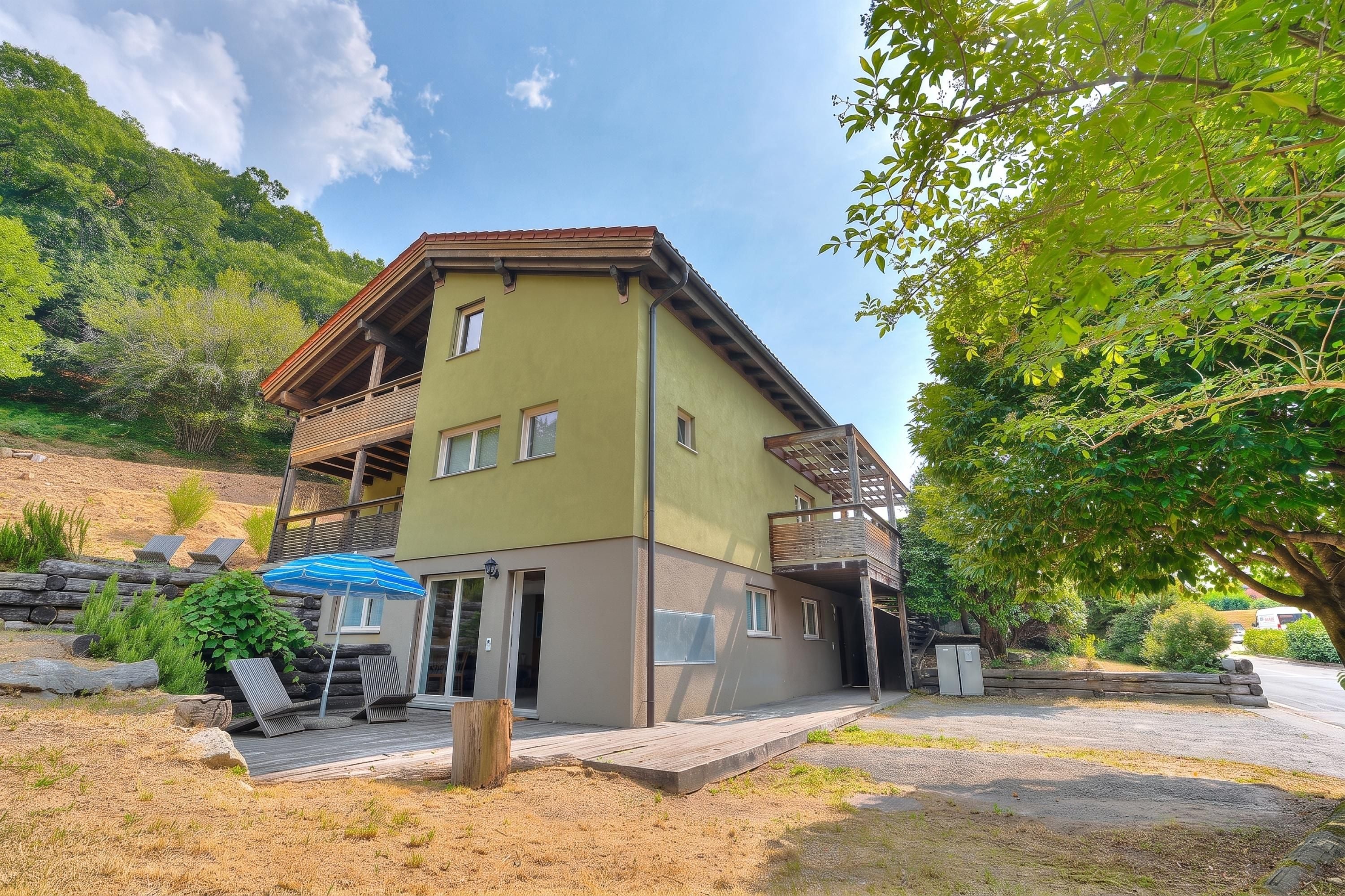 A two-story building with a balcony, a wooden deck, and a blue umbrella.