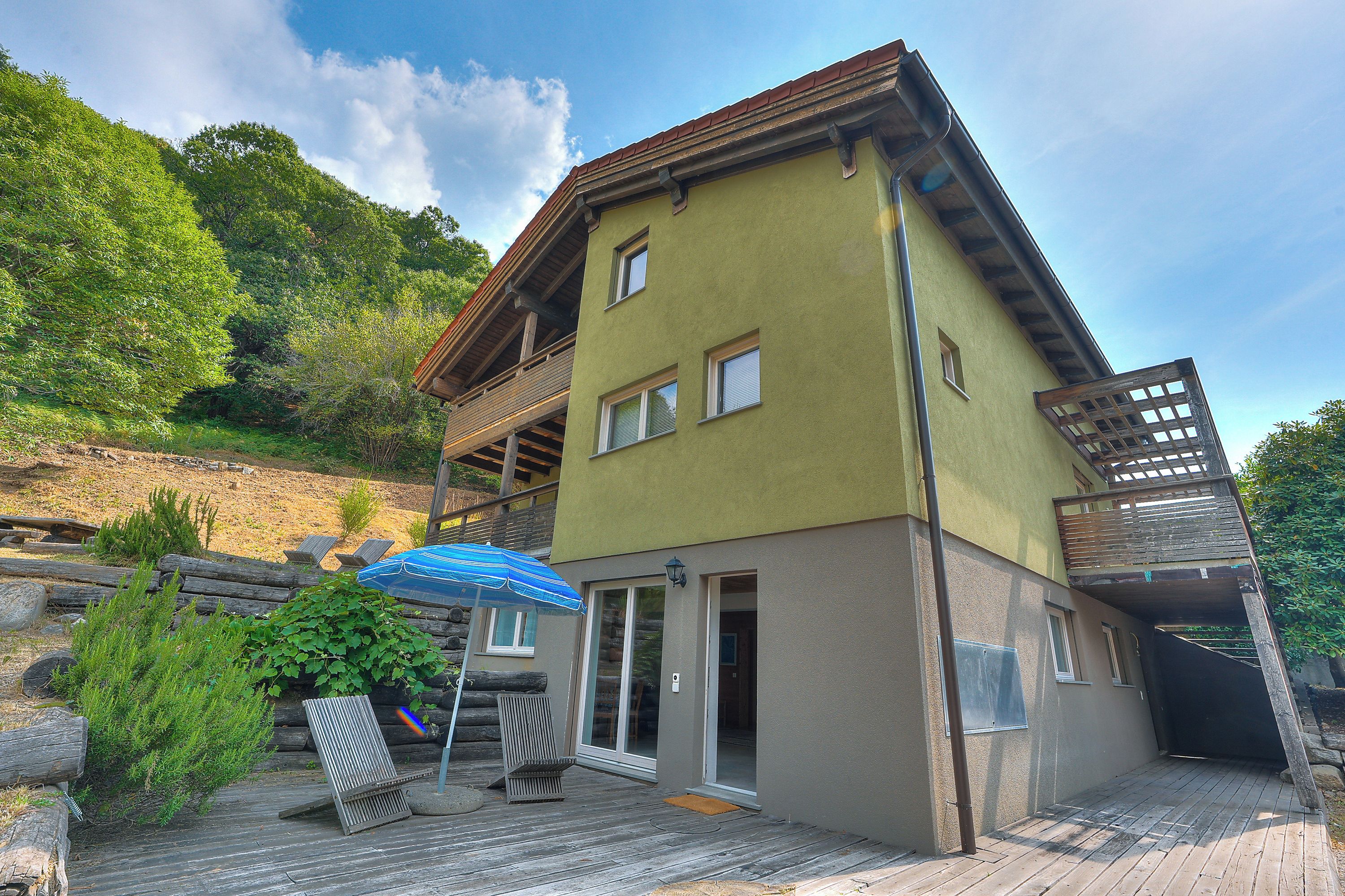 A two-story building with a sloped roof, a balcony, and a wooden deck with lounge chairs.