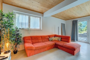 A room with a large sectional sofa, a potted plant, and a window with a view of greenery. - Casa Maamii Mugena With Terrace And Parking (Alto Malcantone)