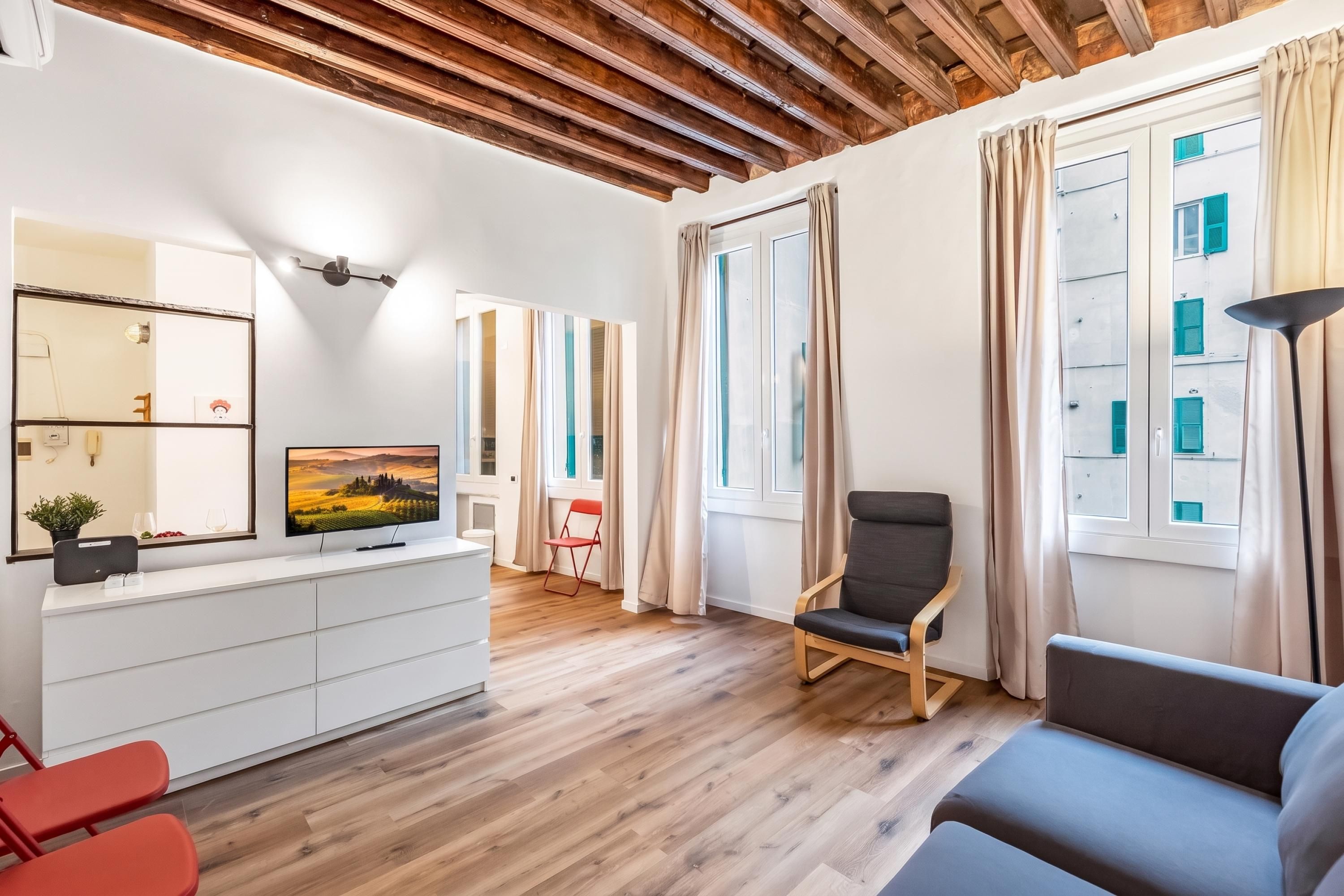 Una sala moderna con techo de madera, un sofá, una silla, un televisor y una ventana con cortinas.