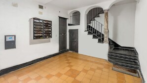 A hallway with a tiled floor, a metal filing cabinet, a door, and a staircase with a metal railing. - Old Town Living in Historic Center & A/C (Genoa)