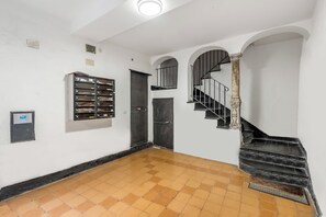 A hallway with a tiled floor, a metal filing cabinet, a door, and a staircase with a metal railing. - Old Town Living in Historic Center & A/C (Genoa)