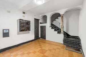Un pasillo con suelo de baldosas, un archivador de metal, una puerta y una escalera con barandilla de metal.
