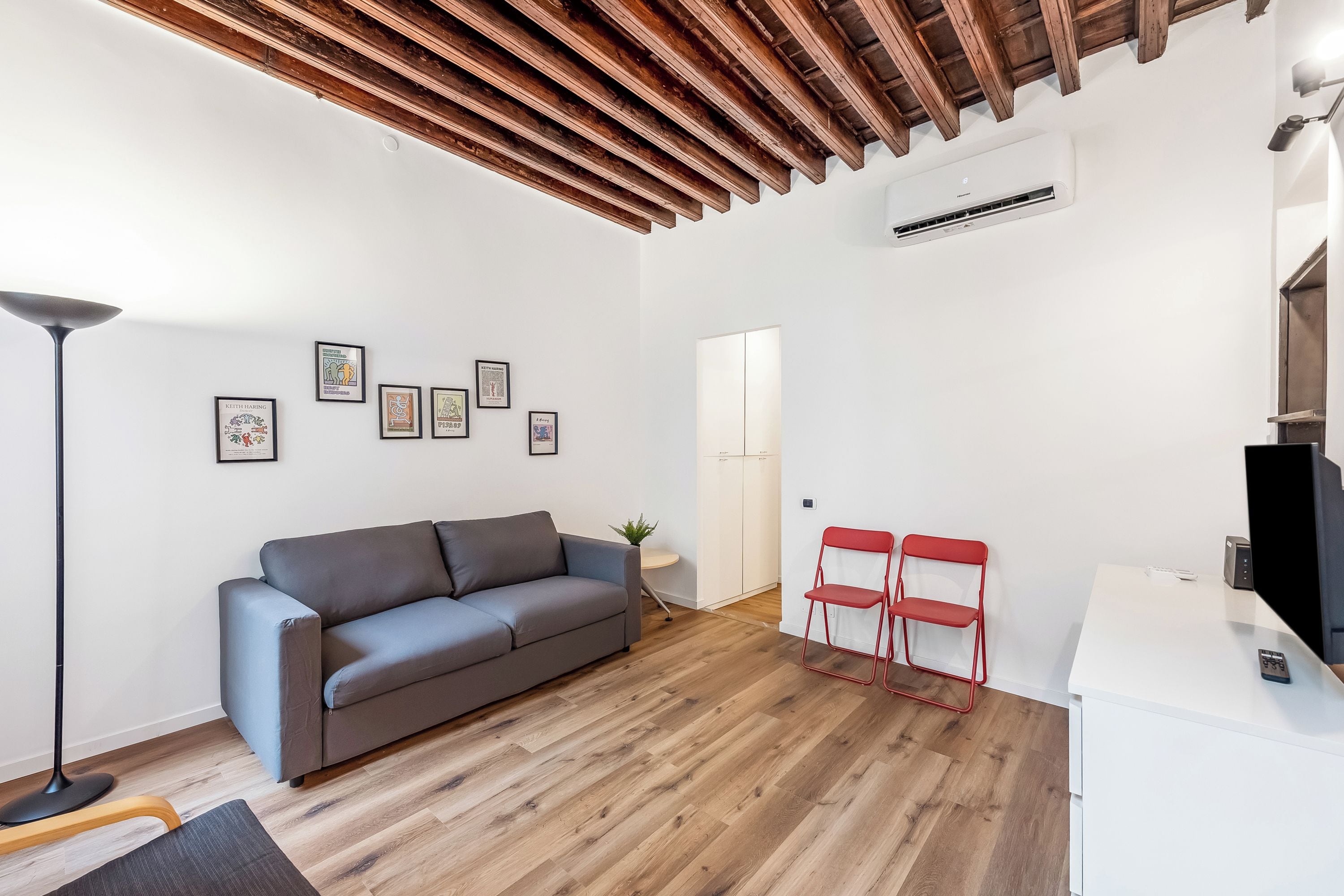 A modern living room with a grey sofa, a wooden ceiling, and a white wall with framed artwork.