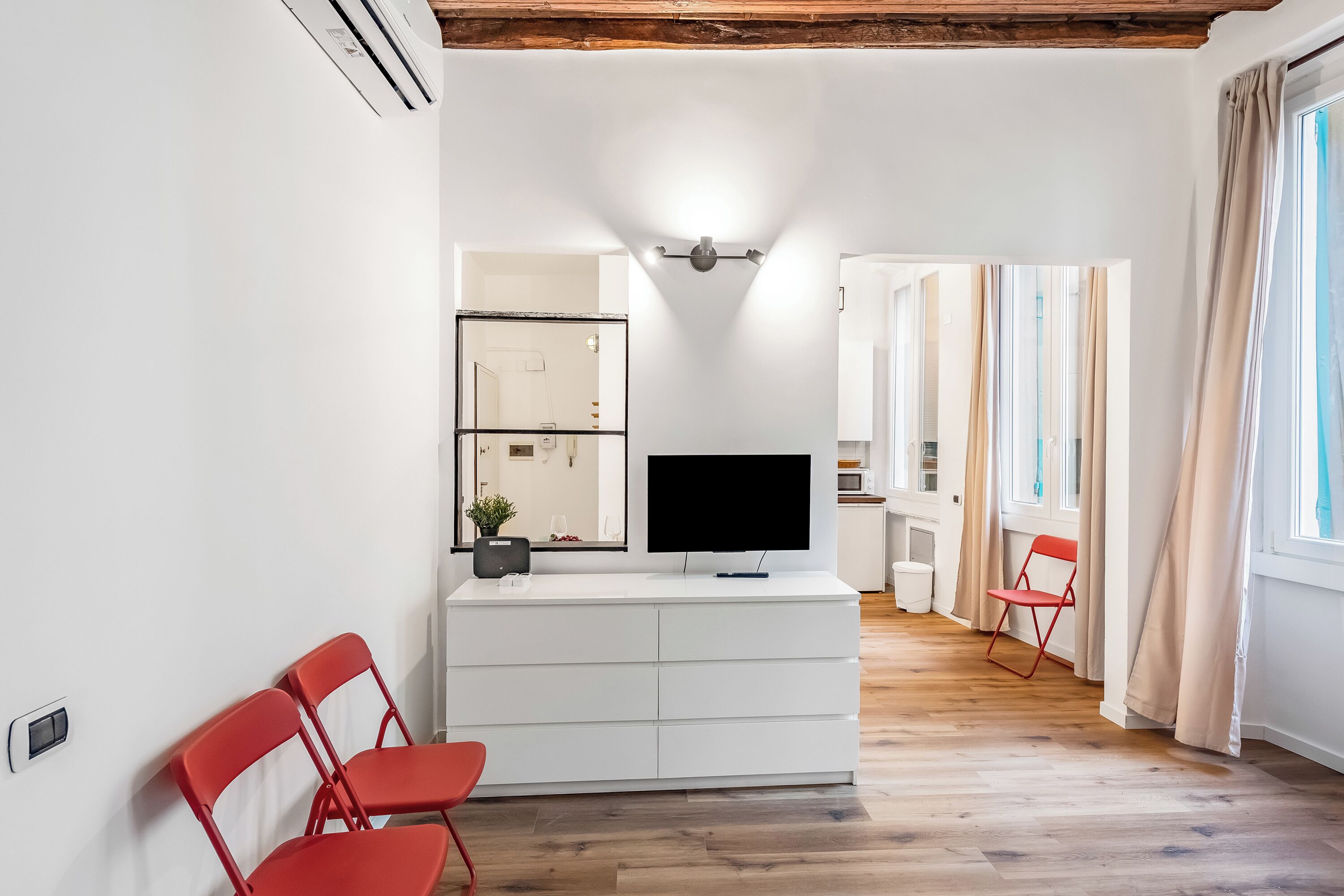 A modern living room with a flat-screen TV, a white cabinet, and a red chair.